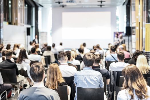 Audience at the conference hall. Copy space on the white screen. Talk at business conference event. Business and Entrepreneurship concept. Focus on unrecognizable people in audience.