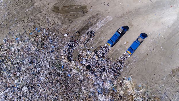 two trash trucks dump waste products polluting our environment in an open landfill
