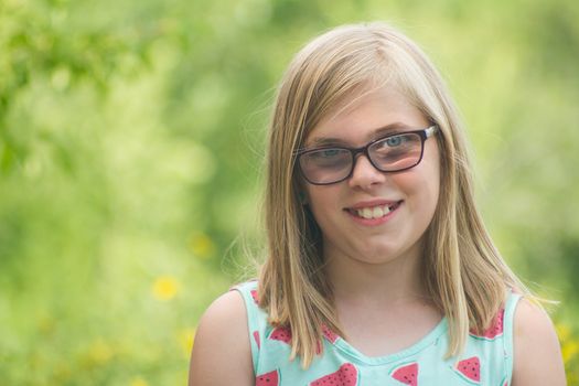 girl smiling with a green blurred background while wearing glasses