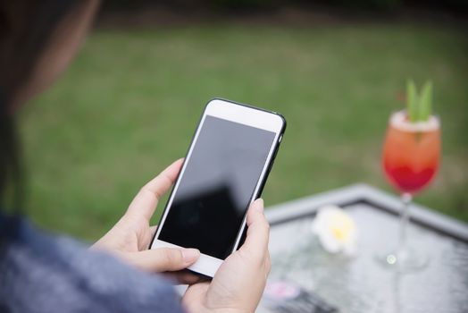 Lady using mobile phone relax in green garden with soft drink background - people and technology lifestyle concept