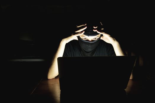 Computer hacker doing his job with laptop computer in the dark room - people with computer criminal concept