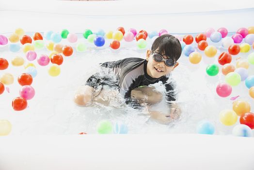 Boy playing with colourful ball in small swimming pool toy - happy boy in water pool toy concept