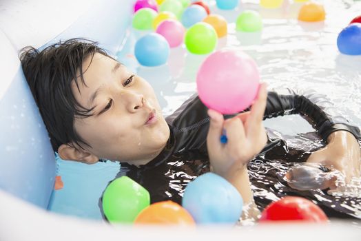 Boy playing with colourful ball in small swimming pool toy - happy boy in water pool toy concept