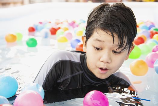 Boy playing with colourful ball in small swimming pool toy - happy boy in water pool toy concept