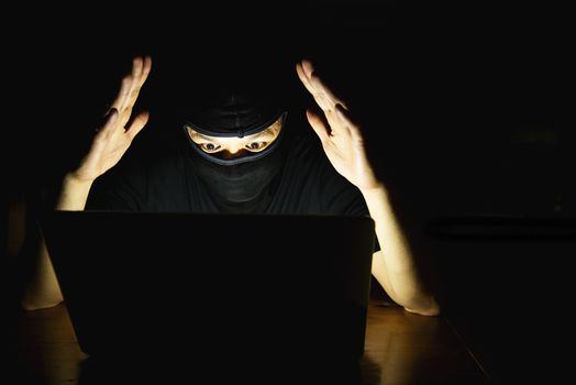 Computer hacker doing his job with laptop computer in the dark room - people with computer criminal concept