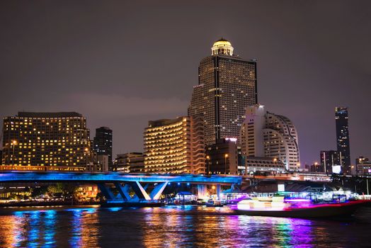 Colorful night picture of Asian city - blue light bridge over big river and building background in Bangkok Thailand