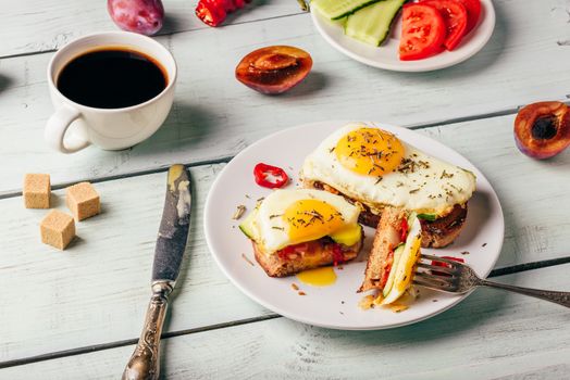 Bruschettas with vegetables and fried egg on white plate, cup of coffee and some fruits over wooden background. Healthy food concept.