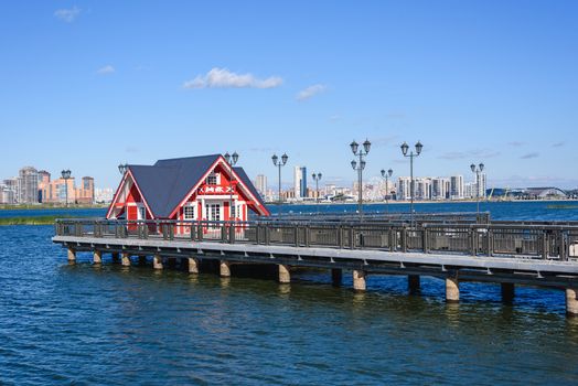 Little red house on pier. High-rises buildings on background.