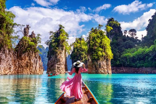 Beautiful girl standing on the boat and looking to mountains in Ratchaprapha Dam at Khao Sok National Park, Surat Thani Province, Thailand.