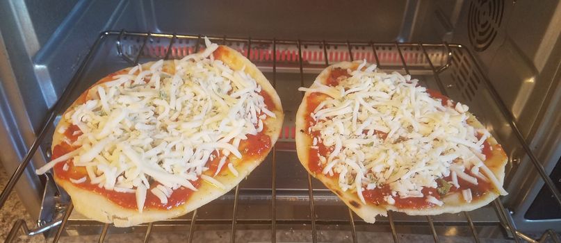 two small pizzas cooking in a toaster oven on a rack