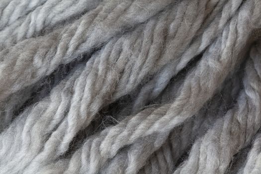 Woolen fluffy threads or tassels from scarf, macro. Soft grey merino wool backdrop, closeup. Autumn and winter flat lay. Scandinavian minimal style.