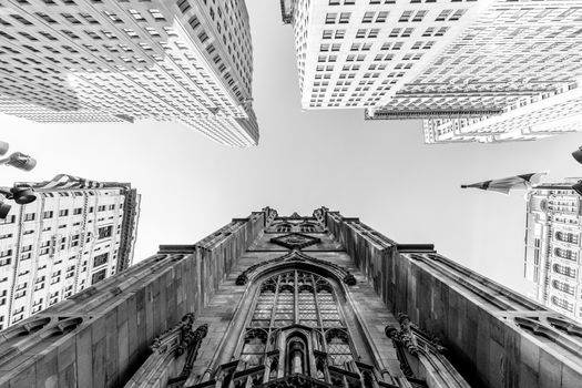 Wide angle upward view of Trinity Church at Broadway and Wall Street with surrounding skyscrapers, Lower Manhattan, New York City, USA. Black and white image.