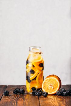 Bottle of Water Infused with Sliced Raw Orange and Fresh Blackberry. Ingredients on Wooden Table.