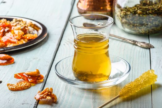 Herbal tea in armudu glass with arabic delights on metal plate over light wooden surface