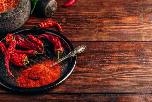 Ground and dried chili peppers on metal plate over wooden surface