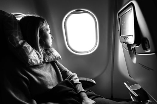 Tired blonde casual caucasian woman sleeping on seat while traveling by airplane on long distance transatlantic flight. Commercial transportation by planes. Black and white image.