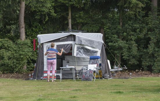 woman busy with installing a roof trailer or folding caravan on a camping in the forest