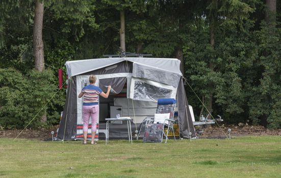 woman busy with installing a roof trailer or folding caravan on a camping in the forest