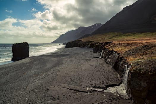 Small waterfall in a black beach in Laekjavik bay, Iceland