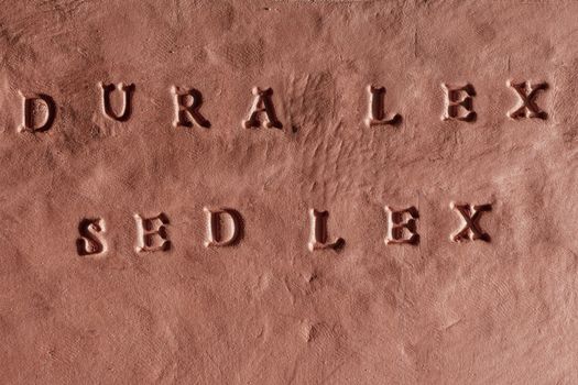 the phrase Dura lex, sed lex written in Latin language on a terracotta tablet