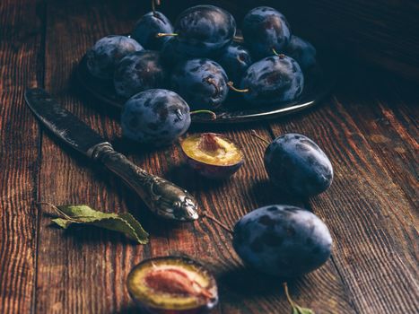 Ripe plums on wooden table with leaves and vintage knife