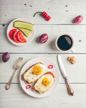 Breakfast toasts with vegetables and fried egg on white plate, cup of coffee and some fruits over wooden background. Clean eating food concept. View from above.