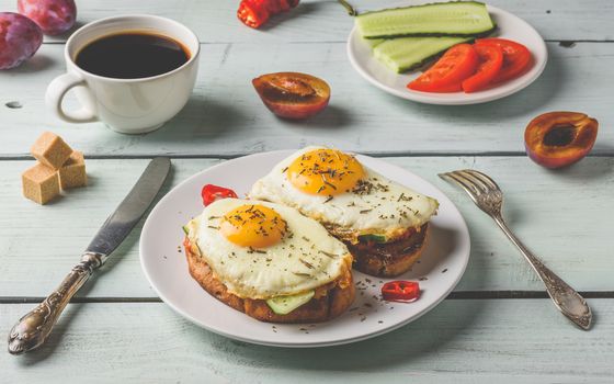 Breakfast toasts with vegetables and fried egg on white plate, cup of coffee and some fruits over wooden background. Clean eating food concept.