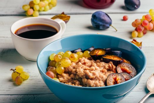 Healthy breakfast concept. Porridge with fresh plum, green grapes and cup of coffee.