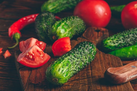 Fresh cucumbers, tomatoes and chili peppers on cutting board for preparing salad.