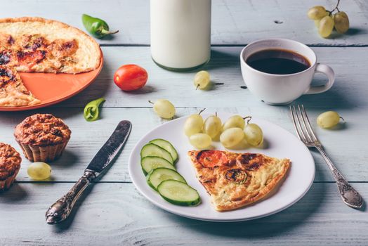 Breakfast frittata with chorizo, tomatoes and chili peppers on plate with cup of coffee, grapes and muffins over light wooden background. Clean eating concept.