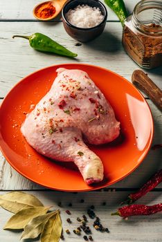 Chicken leg quarter on orange plate over wooden surface with different spices