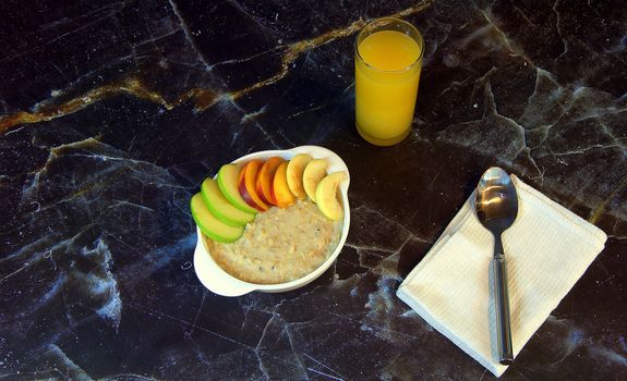 Breakfast, oatmeal with sliced fruit and a glass of orange juice.