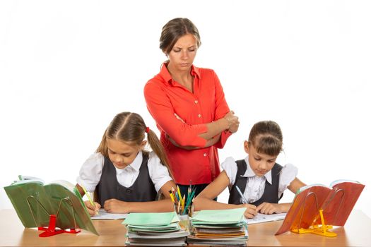 A strict teacher stands above the children who solve the task