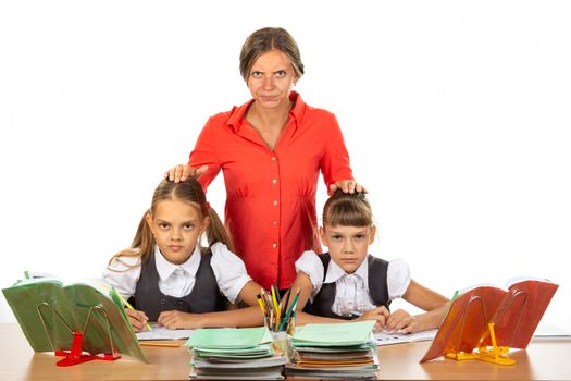 Angry teacher stands behind students sitting at her desk and puts her hands on the heads of children