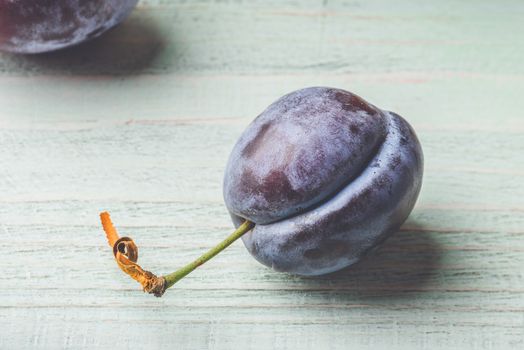 Ripe blue plum on light wooden surface