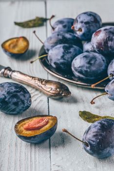 Ripe plums with sliced fruits, leaves and vintage knife over light wooden surface