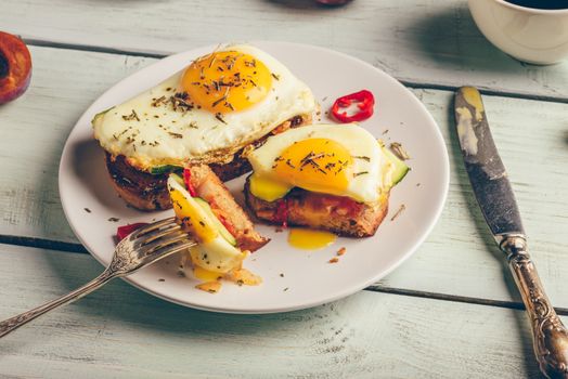 Bruschettas with vegetables and fried egg on white plate, cup of coffee and some fruits over wooden background. Healthy food concept.