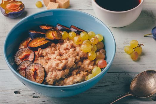 Healthy breakfast concept. Porridge with fresh plum, green grapes and cup of coffee.