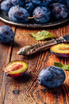 Ripe plums on wooden table with leaves, water drops and vintage knife