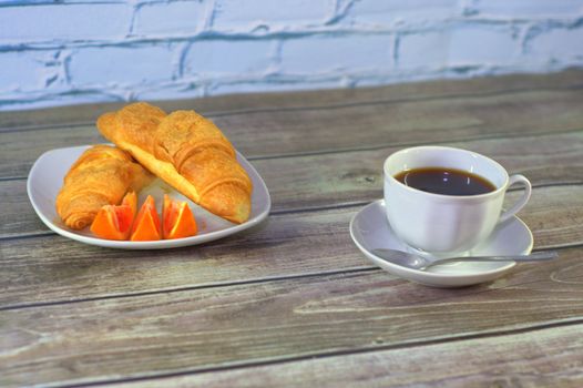 light breakfast, black coffee, two croissants and slices of orange.