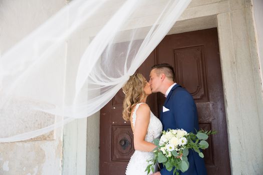 The Kiss. Bride and groom kisses tenderly in the shadow of a flying veil. Close up portrait of sexy stylish wedding couple kissing under white vail.