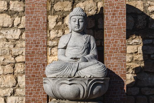 White stone statue of a Buddha on masonry background