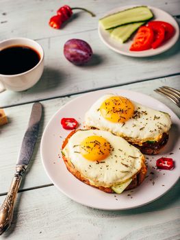 Breakfast toasts with vegetables and fried egg on white plate, cup of coffee and some fruits over wooden background. Clean eating food concept.