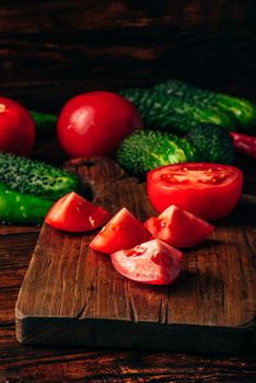 Sliced tomatoes on cutting board and cucumbers with chili peppers over wooden background.