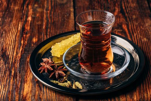 Spiced tea in oriental glass with star anise and green cardamom with navad on metal tray over wooden surface