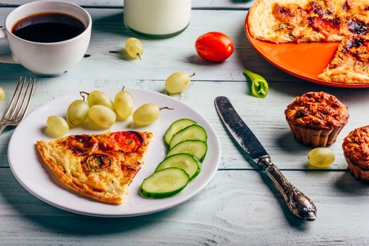 Slice of frittata with cup of coffee, grapes and muffins over light wooden background. Healthy eating concept.