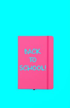 Back to school handwritten sign on pink leather cover notebook over blue paper background with copy space