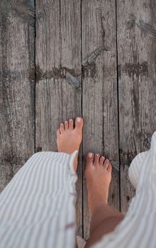 Beautiful female bare bare tanned legs with pink pedicure on wooden beach flooring. Top view, copy space.