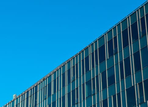 Upper part of modern glass office building diagonally, blue sky in the background.