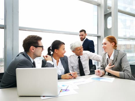 Business team sitting by the table with laptop and documents in office